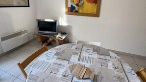 Ett rum med ett runt bord täckt av tidningar, en tv på ett stativ och en stor, abstrakt målning på väggen.