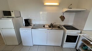 Ett kompakt kök med kylskåp, mikrovågsugn, kaffebryggare, diskho och spis.