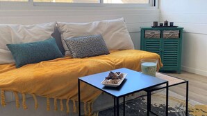 A cozy room with a sofa, a small table, and a window with a view of trees and a house. - Combrit, nice duplex with heated pool, tennis court and beach on foot (COMBRIT)