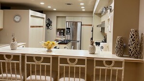 Une cuisine moderne dotée d’un îlot central, d’appareils électroménagers en acier inoxydable et d’un coin repas avec des chaises blanches.