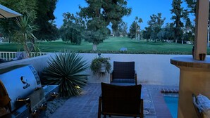 Une terrasse extérieure équipée d’un barbecue, de sièges et offrant une vue sur un terrain de golf.