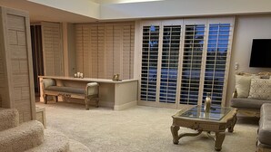 Un vaste salon doté d’un haut plafond, d’une grande fenêtre avec stores, d’un escalier et d’un téléviseur à écran plat fixé au mur.