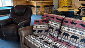 A cozy cabin interior with a leather sofa, wooden walls, a bar area, and a dining table. - Hide a way in our Lodge that sleeps 18! (Indian River)