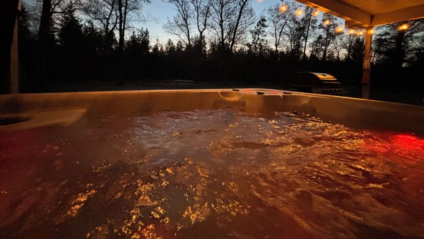 A hot tub with water, surrounded by trees and string lights. - Hide a way in our Lodge that sleeps 18! (Indian River)