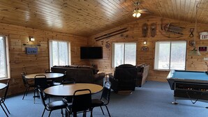A cozy cabin interior with a pool table, a sofa, and a television. - Hide a way in our Lodge that sleeps 18! (Indian River)