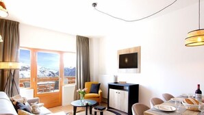 Una sala moderna con sofá, mesa de centro y comedor. Se ve una vista de montañas a través de ventanas amplias.