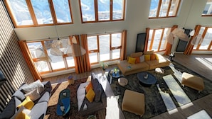 Un salón amplio con ventanas grandes, un conjunto de sofás, una mesa de centro y una lámpara colgante.