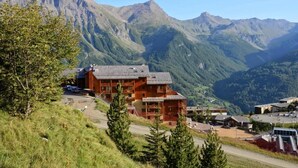 Un chalet de montagne à l’extérieur en bois, doté de plusieurs balcons et offrant une vue sur les montagnes environnantes.