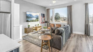 A modern living room with a sofa, a coffee table, a TV, and a bookshelf. - 2 Premier Nashville Homes • Sleeps 24 • Rooftops (Nashville)