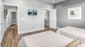 A bedroom with two beds, a ceiling fan, a TV, and a bathroom visible through an open door. - 2 Premier Nashville Homes • Sleeps 24 • Rooftops (Nashville)