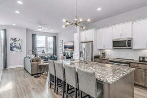 A modern kitchen with white cabinets, a stainless steel refrigerator, and a marble island with bar stools.