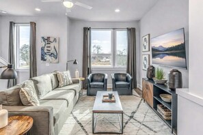 A modern living room with a sofa, two armchairs, a coffee table, and a TV on a stand.