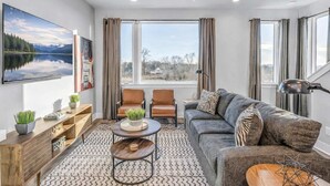 A modern living room with a large flat-screen TV, a sofa, two armchairs, a coffee table, and a ceiling fan. - 2 Premier Nashville Homes • Sleeps 24 • Rooftops (Nashville)