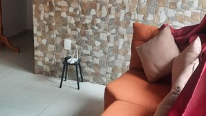 Una sala de estar con pared de piedra, un televisor de pantalla plana, un sofá y una pequeña mesa con una silla.