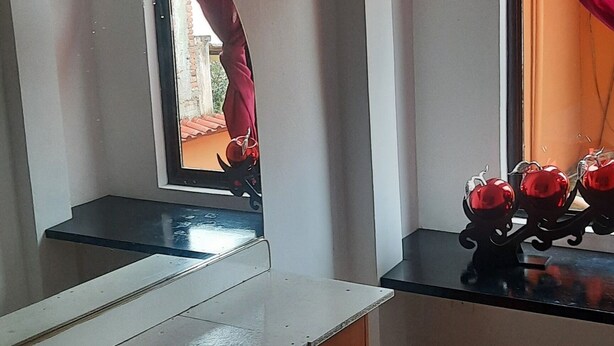 Una habitación con un escritorio de madera, un espejo, una ventana con cortinas rojas y suelo de baldosas.