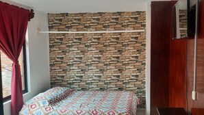 Un dormitorio con pared de diseño de piedra, cama con ropa de cama estampada y un armario de madera.