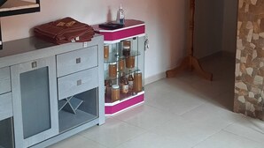Una habitación con una escalera, un perchero de madera, un armario rosa y blanco con botellas y una pared de piedra.