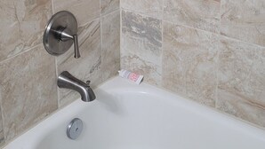 Une salle de bain avec une baignoire blanche, un robinet mural et des carreaux de marbre beige.
