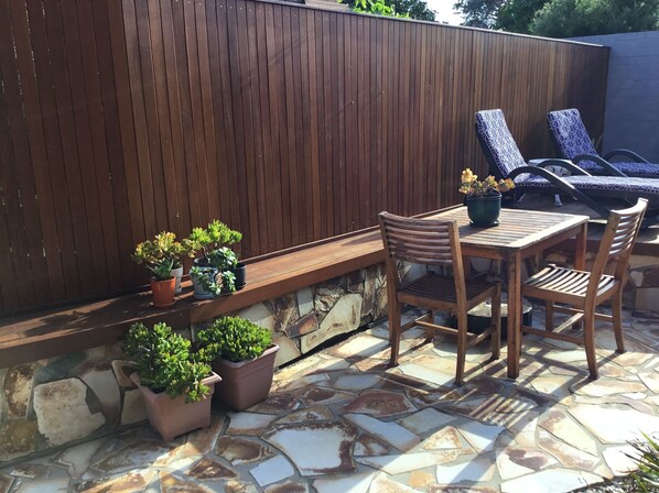 A patio area with a wooden table and chairs, a stone floor, and potted plants.