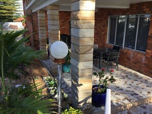 A covered outdoor area with stone pillars, a table and chairs, and potted plants.