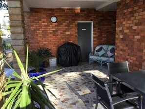 A patio area with a brick wall, a covered grill, a cushioned outdoor seating, and a tiled floor.