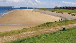 Ein Strand mit einer langen, schmalen Wasserfläche, einer Grünfläche und einem Gebäude mit Flachdach.