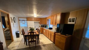 A compact kitchen with wooden cabinets, a dining table with chairs, a refrigerator, a microwave, and a television. - Cottage near the Bay (Crisfield)
