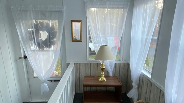 A room with a wooden bench, a lamp, a wicker basket, and a window with sheer curtains. - Cottage near the Bay (Crisfield)