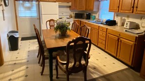 A kitchen with wooden cabinets, a dining table with chairs, a refrigerator, a microwave, and a sink. - Cottage near the Bay (Crisfield)