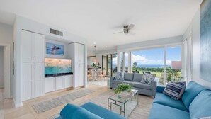 Un ampio soggiorno con una grande TV, un divano grigio e vista sull'oceano.