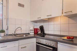 Eine moderne Küche mit weißen Schränken, einer Edelstahlspüle, einer Kaffeemaschine und einer Tomatenschale auf der Arbeitsplatte.
