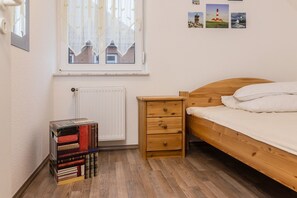 Ein Schlafzimmer mit einem hölzernen Bett, einem Nachttisch mit Büchern, einer Heizung und einem Fenster mit Vorhängen.