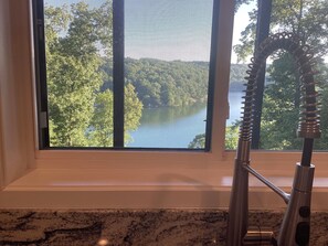 A kitchen with a window overlooking a forested area and a lake.