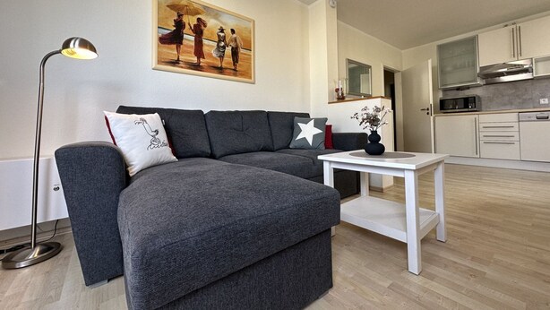 A modern living room with a grey sectional sofa, a white coffee table, and a painting on the wall. - Strandhausvilla Wo. 2 - "Strandhausvilla - Whg.2" Beach chair included! (Dahme)