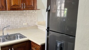 A kitchen with wooden cabinets, a stainless steel refrigerator, a sink, and a patterned backsplash. - LOVELY TWO BEDROOMS , TWO BATHROOMS IN HIGUEY (Higüey)