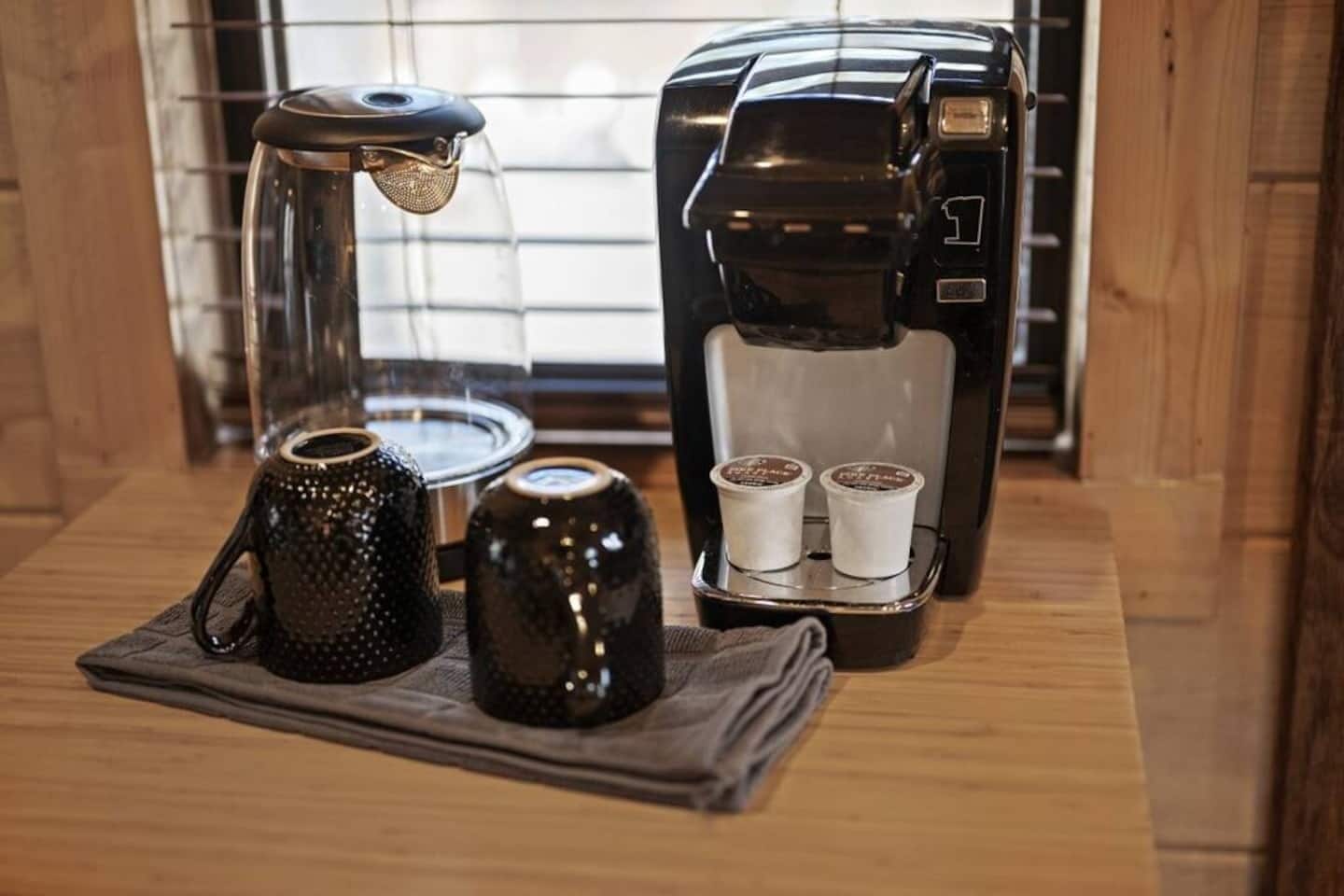 Een koffiezetapparaat met twee koffiekapsules en een waterkoker op een houten tafel.