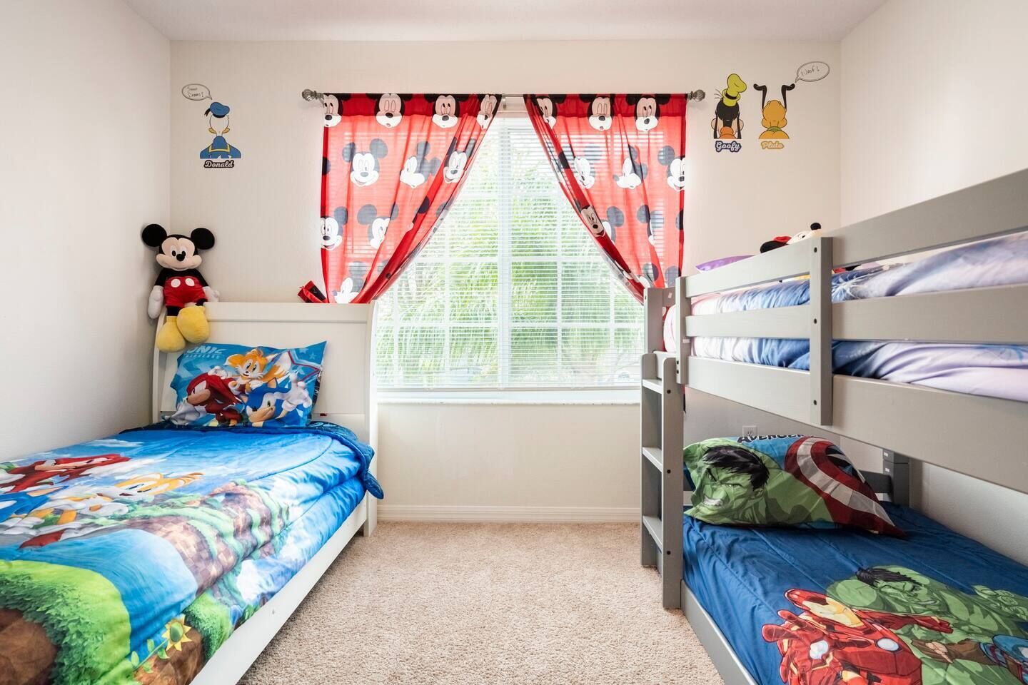 Een kinderkamer met stapelbedden, een Mickey Mouse knuffel en beddengoed met tekenfilms.
