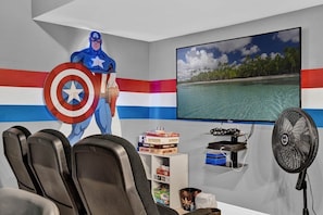 A room with a Captain America figure, a TV displaying a beach scene, a fan, and a shelf with items.