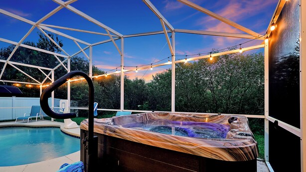 Una banyera d'hidromassatge amb revestiment de fusta, una piscina i llums penjants en una zona exterior coberta.