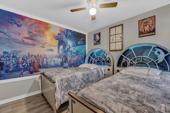 A bedroom with two beds, a large mural on the wall, and a ceiling fan.