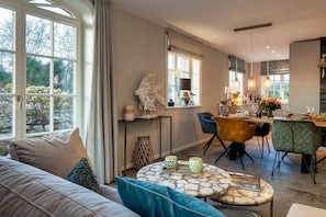 Ein modernes Wohnzimmer mit einer Couch, einem Essbereich mit Stühlen, einer Küche mit Esstisch und großen Fenstern.