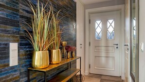 Un couloir avec un mur à texture, une console en bois ornée de vases et une porte blanche avec une fenêtre.