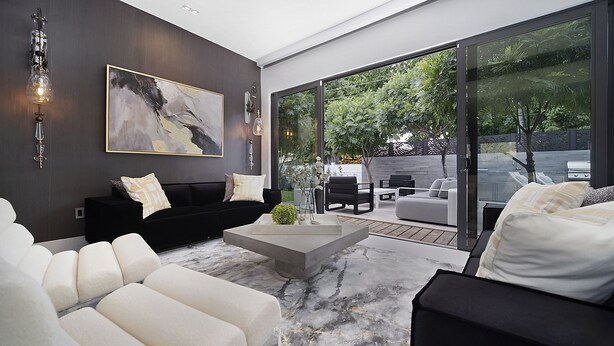 A modern living room with a black sofa, white armchairs, and a large glass door leading to an outdoor patio. - Private Saltwater Pool - Updated Modern 3BR 3BA - 1 Mile to Beach! (Fort Lauderdale)