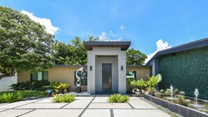 A modern building with a central entrance, paved courtyard, and surrounding greenery. - Private Saltwater Pool - Updated Modern 3BR 3BA - 1 Mile to Beach! (Fort Lauderdale)
