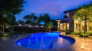 A swimming pool with a curved edge, surrounded by a landscaped area with trees and a building with large windows. - Private Saltwater Pool - Updated Modern 3BR 3BA - 1 Mile to Beach! (Fort Lauderdale)