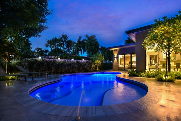 A swimming pool with a curved edge, surrounded by a landscaped area with trees and a building with large windows. - Private Saltwater Pool - Updated Modern 3BR 3BA - 1 Mile to Beach! (Fort Lauderdale)