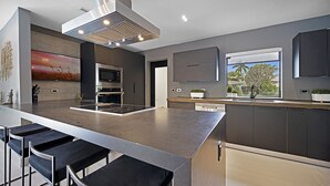 A modern kitchen with a central island, built-in appliances, and a large window offering a view of the outdoors. - Private Saltwater Pool - Updated Modern 3BR 3BA - 1 Mile to Beach! (Fort Lauderdale)