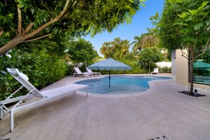 A swimming pool with lounge chairs and an umbrella, surrounded by greenery and a modern building. - Private Saltwater Pool - Updated Modern 3BR 3BA - 1 Mile to Beach! (Fort Lauderdale)
