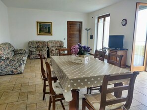 A dining area with a table set for four, surrounded by floral-patterned sofas and a television in the background.