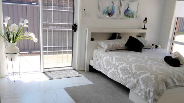 Ein Schlafzimmer mit einem Bett, einer Tür zu einem Balkon, einem kleinen Tisch mit einer Blumenvase und einer Wand-Klimaanlage.